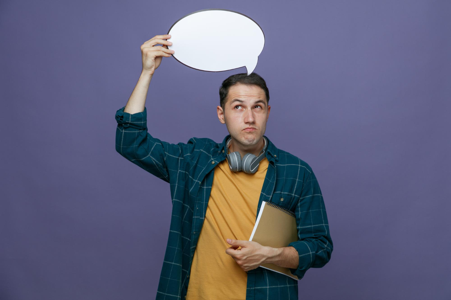 thoughtful-young-male-student-wearing-headphones-around-neck-holding-note-pad-arm-chat-bubble-head-looking-up-isolated-purple-background